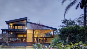 A modern two-story house with a large glass facade, outdoor seating area, and a well-maintained garden. - The Banks: Luxury waterfront retreat on Currambene Creek Jervis Bay (Woollamia)