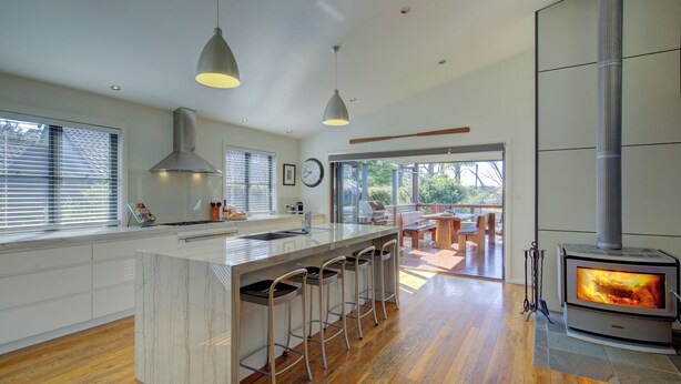 A modern kitchen with a central island, bar stools, a large stove, and a view to an outdoor patio. - The Banks: Luxury waterfront retreat on Currambene Creek Jervis Bay (Woollamia)