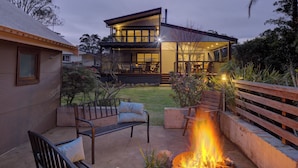 A modern house with a fire pit in the backyard, outdoor seating, and a well-lit patio area. - The Banks: Luxury waterfront retreat on Currambene Creek Jervis Bay (Woollamia)
