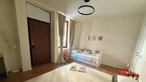 A bedroom with a bed, a nightstand, a chair, a window with curtains, a radiator, and a door.