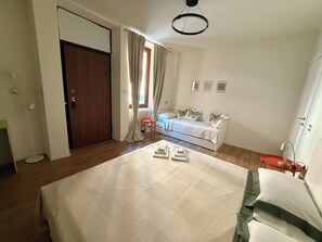 Ein Schlafzimmer mit einem Bett, einem Nachttisch, einem Sessel, einem Fenster mit Vorhängen, einem Heizkörper und einer Tür.