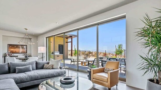 Ein modernes Wohnzimmer mit Sofa, Sessel und Couchtisch, großen Fenstern und Blick ins Freie.