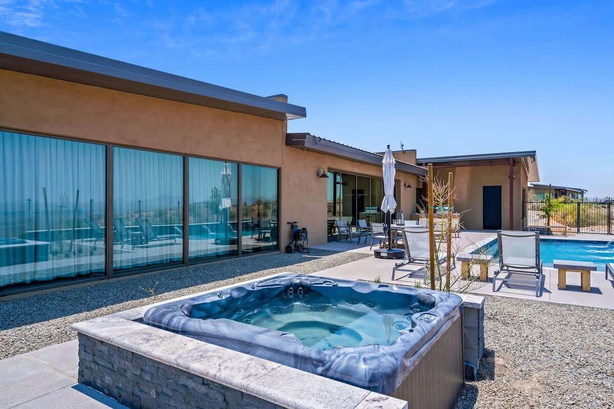 A modern house with a swimming pool, a hot tub, and a patio area with outdoor furniture.