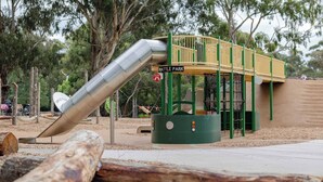 Un parque infantil con un tobogán y estructuras para escalar, rodeado de árboles.