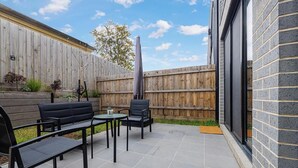 Un patio con cerco de madera, una parrilla y mobiliario exterior.