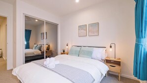 Un dormitorio con una cama grande, un armario, dos mesitas de noche con lámparas y un espejo.