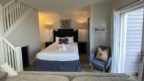 A bedroom with a bed, a chair, a nightstand, a lamp, a sign, and a staircase.