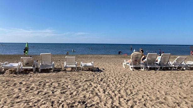 A beach with rows of white lounge chairs and a few people in the water.