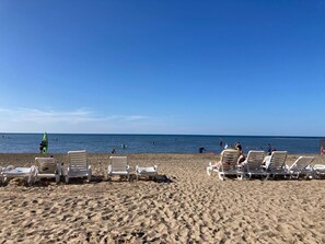 Une plage bordée de rangées de chaises longues blanches, avec quelques personnes dans l’eau.