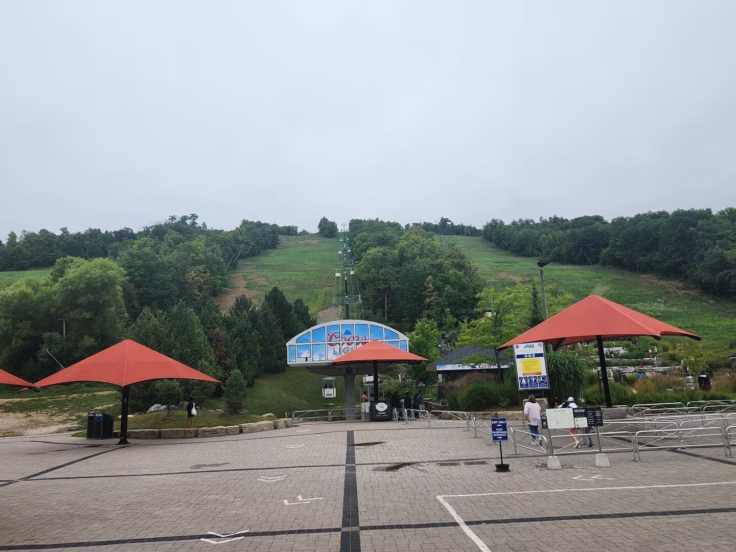 A parking area with red umbrellas, a blue building, and a grassy hill in the background.