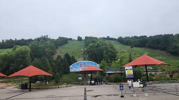 A parking area with red umbrellas, a blue building, and a grassy hill in the background.