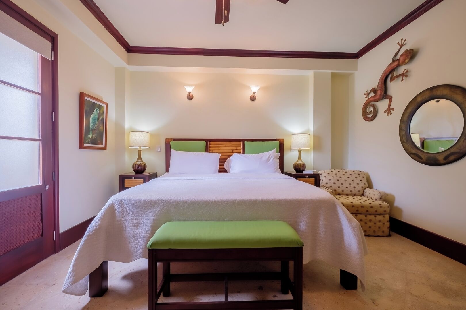 Un letto rifatto con cura, una panca verde, due lampade da comodino, una cornice con un'immagine e un elemento decorativo a parete in una camera d'albergo.