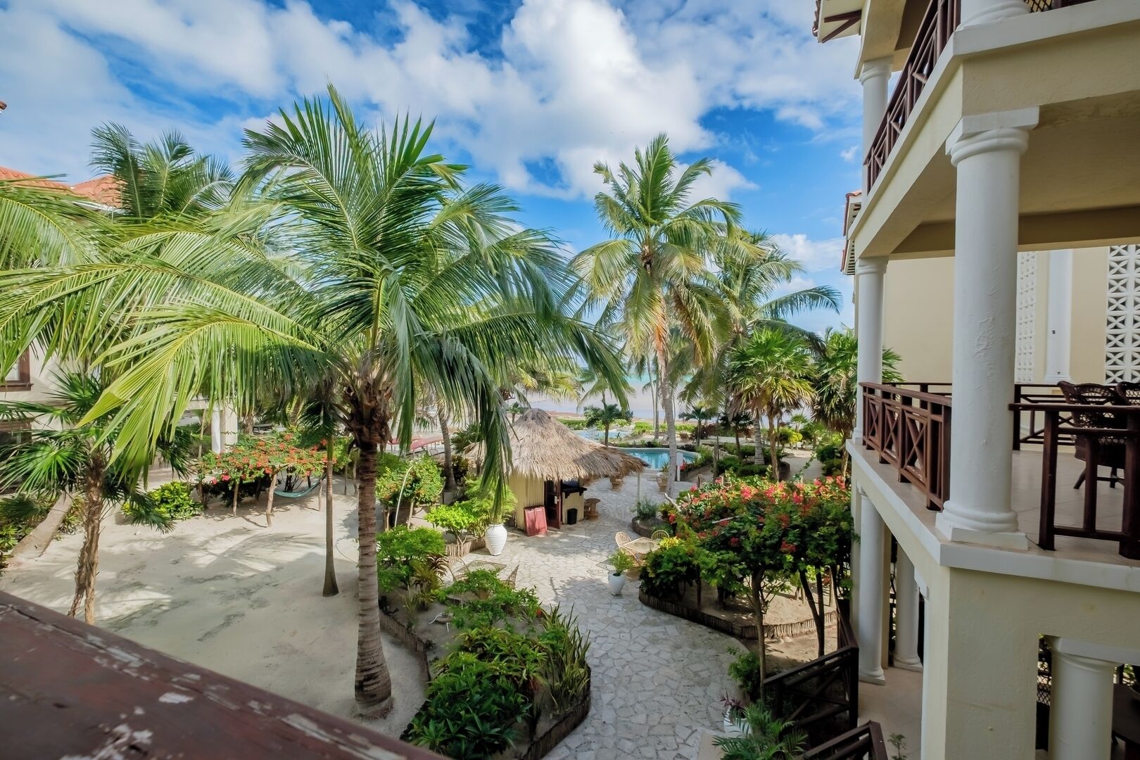 A courtyard with palm trees, a pool, and a building with a balcony.