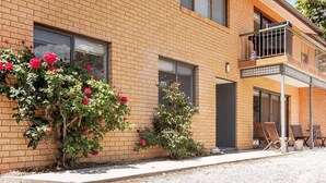Een modern gebouw van baksteen met een balkon, een grindpad en een kleine tuin met rode bloemen.