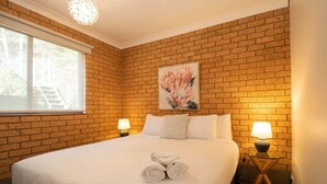 Een hotelkamer met een bakstenen muur, een groot bed met witte lakens, twee bedlampen en een schilderij van bloemen aan de muur.