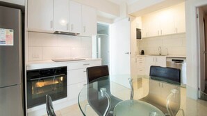 Een moderne keuken met witte kasten, roestvrijstalen apparatuur en een glazen eettafel.