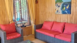 Una habitación con un sofá y sillones de mimbre, una mesita con una planta y un cuadro en la pared.