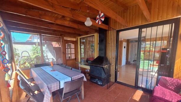 Un interior de madera con una mesa de comedor, sillas, una parrilla y un ventanal corredero que da a un espacio exterior.