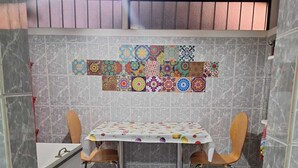 Un comedor con una mesa cubierta por un mantel floral, dos sillas y una pared decorativa con azulejos estampados.