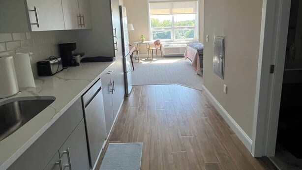 A modern kitchen with stainless steel appliances, a dining area with a table and chairs, and a large window providing natural light. - 410 Modern Brand New Studio Apartment (Old Bridge)