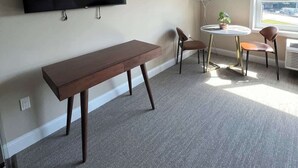 A room with a flat-screen TV mounted on the wall, a wooden bench, two chairs, a small round table with a lamp, and a large window providing a view outside. - 410 Modern Brand New Studio Apartment (Old Bridge)