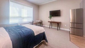 A bedroom with a bed, a desk, a chair, a TV, and a refrigerator. - 411 Modern Brand New Studio Apartment (Old Bridge)