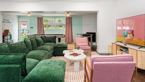 Un salon moderne avec un canapé d’angle vert, un fauteuil rose, une table basse blanche et un téléviseur à écran plat posé sur un meuble en bois.