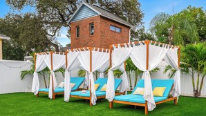 Un jardin avec quatre chaises longues bleues placées sous des auvents blancs, une maison en briques en arrière-plan et une clôture blanche.