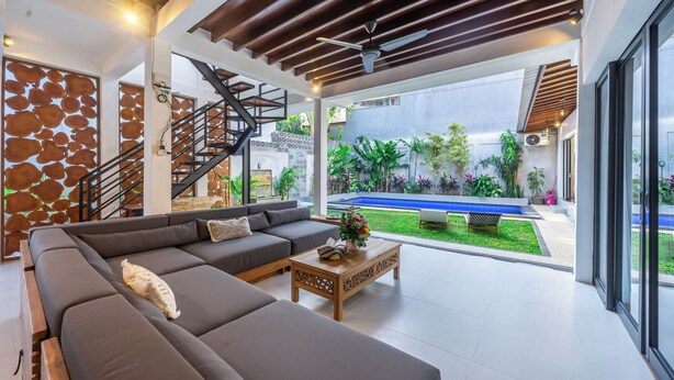 Uma sala de estar moderna com um amplo sofá modular, uma mesa de centro de madeira e uma escada que leva a uma área externa com piscina.