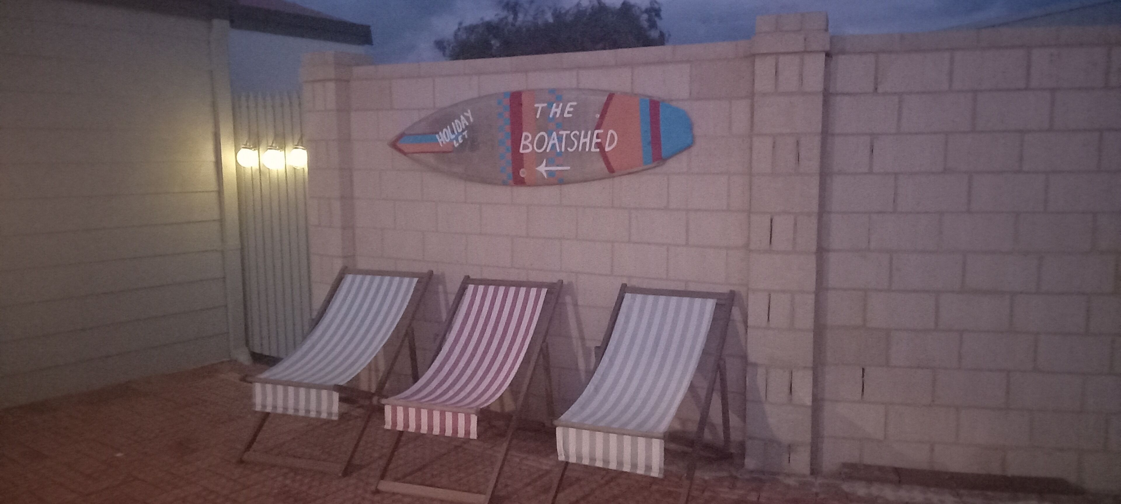 A beachside area with a sign reading "The Boathouse" and three striped lounge chairs.