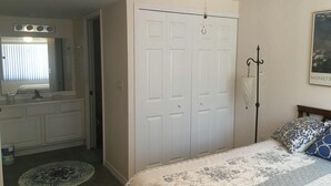 Ein Schlafzimmer mit Bett, einem weißen Kleiderschrank, einem Badezimmer mit Waschbecken und Spiegel sowie einem Bild an der Wand.