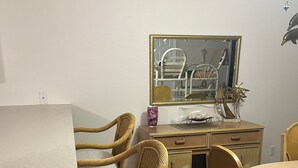 Ein Essbereich mit einem runden Tisch, vier Korbstühlen, einer Kommode mit Spiegel und einer Vase darauf.