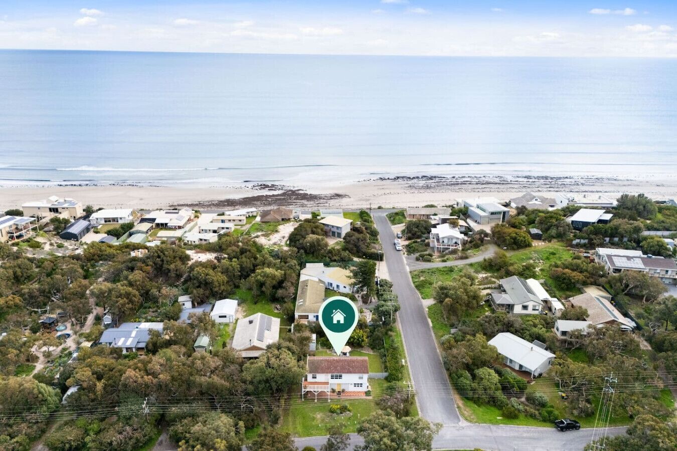 An aerial view of a coastal residential area with houses, a beach, and a road leading to the sea.
