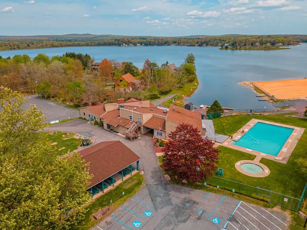 A lakeside property with a swimming pool, a covered parking area, and a building with a red roof.