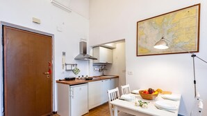 Cocina compacta con armarios blancos, encimera de madera y comedor con una mesa para dos.