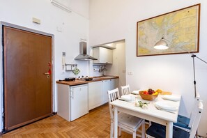 Cocina compacta con armarios blancos, encimera de madera y comedor con una mesa para dos.