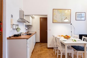 A modern kitchen with white cabinets, a wooden countertop, and a built-in stove. There is a dining area with a white table, chairs, and a map on the wall.