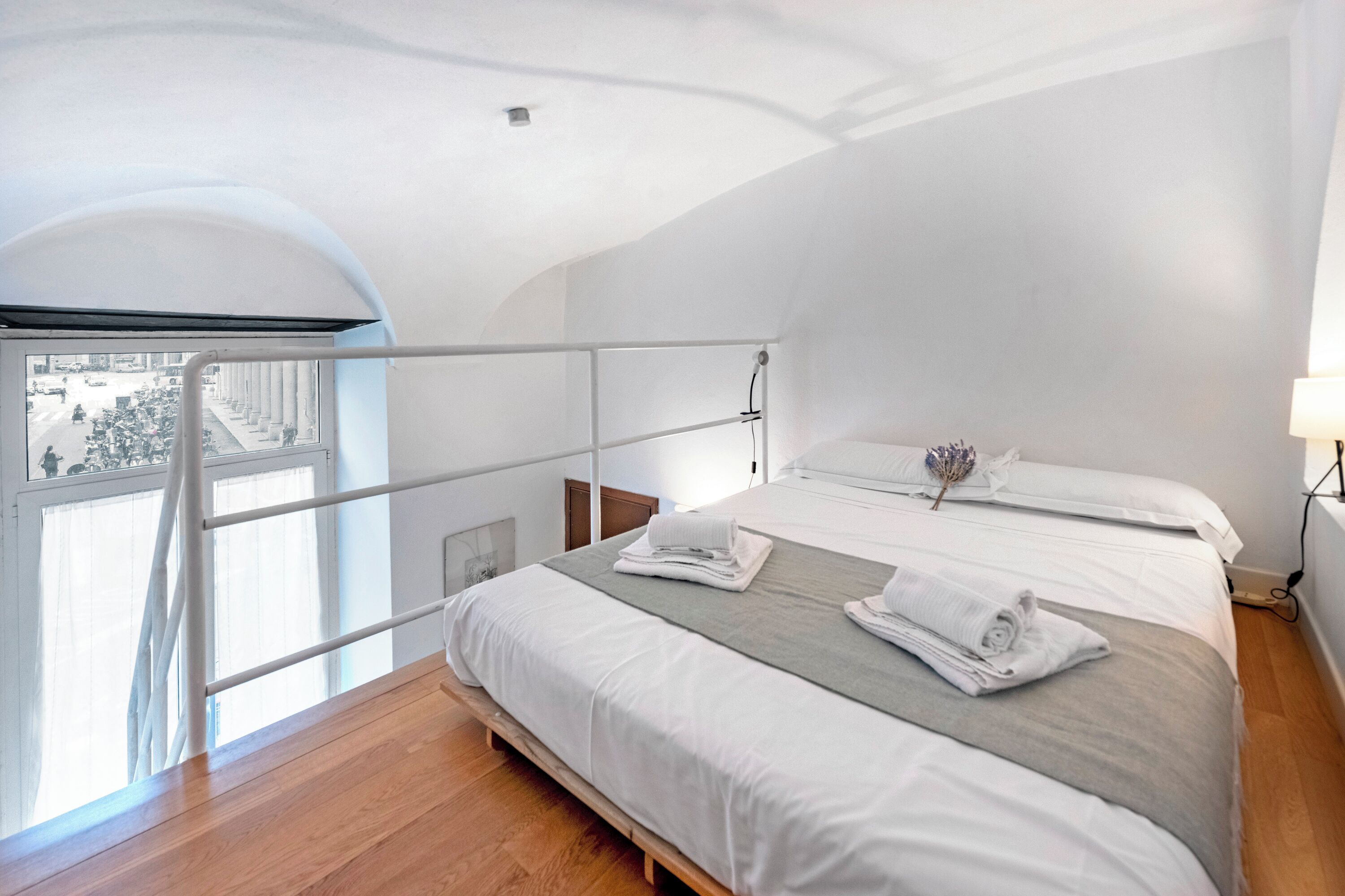 Un dormitorio moderno con una cama grande, un ventanal con vista a la calle y un balcón.