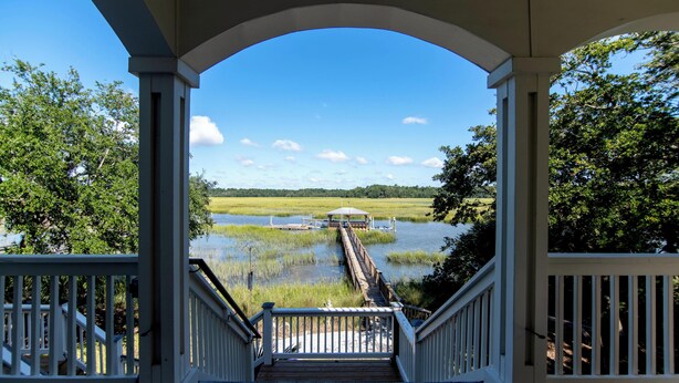A wooden deck with a view of a dock extending into a body of water, surrounded by greenery.