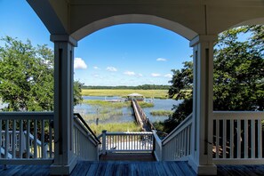 A wooden deck with a view of a dock extending into a body of water, surrounded by greenery.