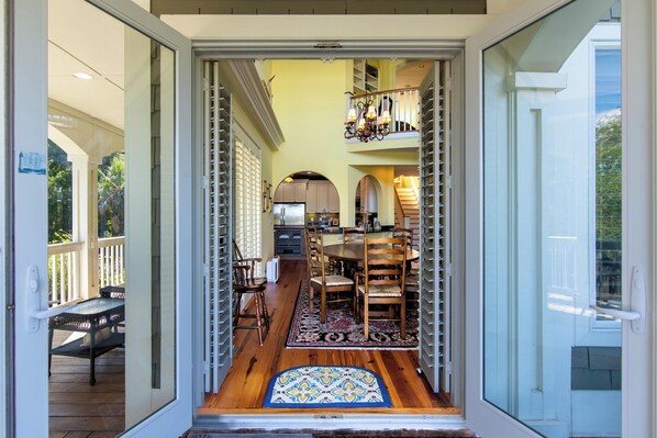 A spacious dining area with a wooden table and chairs, a patterned rug, and a view of the kitchen and upper level.