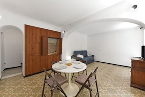 A dining area with a round table, chairs, and a sofa in the background.