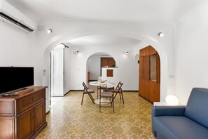 Ein modernes Wohnzimmer mit Flachbildfernseher, einem blauen Sofa und einem Essbereich mit rundem Tisch und Stühlen.