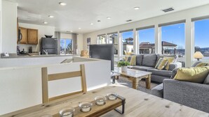 A modern kitchen with wooden cabinets and a large island, a living area with a gray sofa and a coffee table, and large windows offering a view of the surrounding area. - Whole Duplex! 3 Bedrooms, 2 Bathrooms, 4 Beds, Sleeps 8 (Colorado Springs)