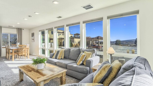 A spacious living room with a grey sofa, wooden coffee table, and large windows offering a view of the surrounding buildings. - Whole Duplex! 3 Bedrooms, 2 Bathrooms, 4 Beds, Sleeps 8 (Colorado Springs)