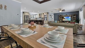 A modern living room with a dining area, a kitchen in the background, and a television on the right.