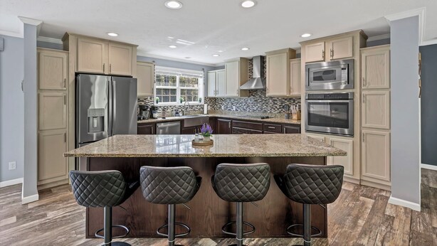 A modern kitchen with a granite island, stainless steel appliances, and dark wood flooring.