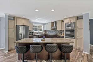 A modern kitchen with a granite island, stainless steel appliances, and dark wood flooring. - 5BR Getaway - Hot Tub, Sauna, Pool Table, Game Room & 75" TV with Scenic Views (Logan)