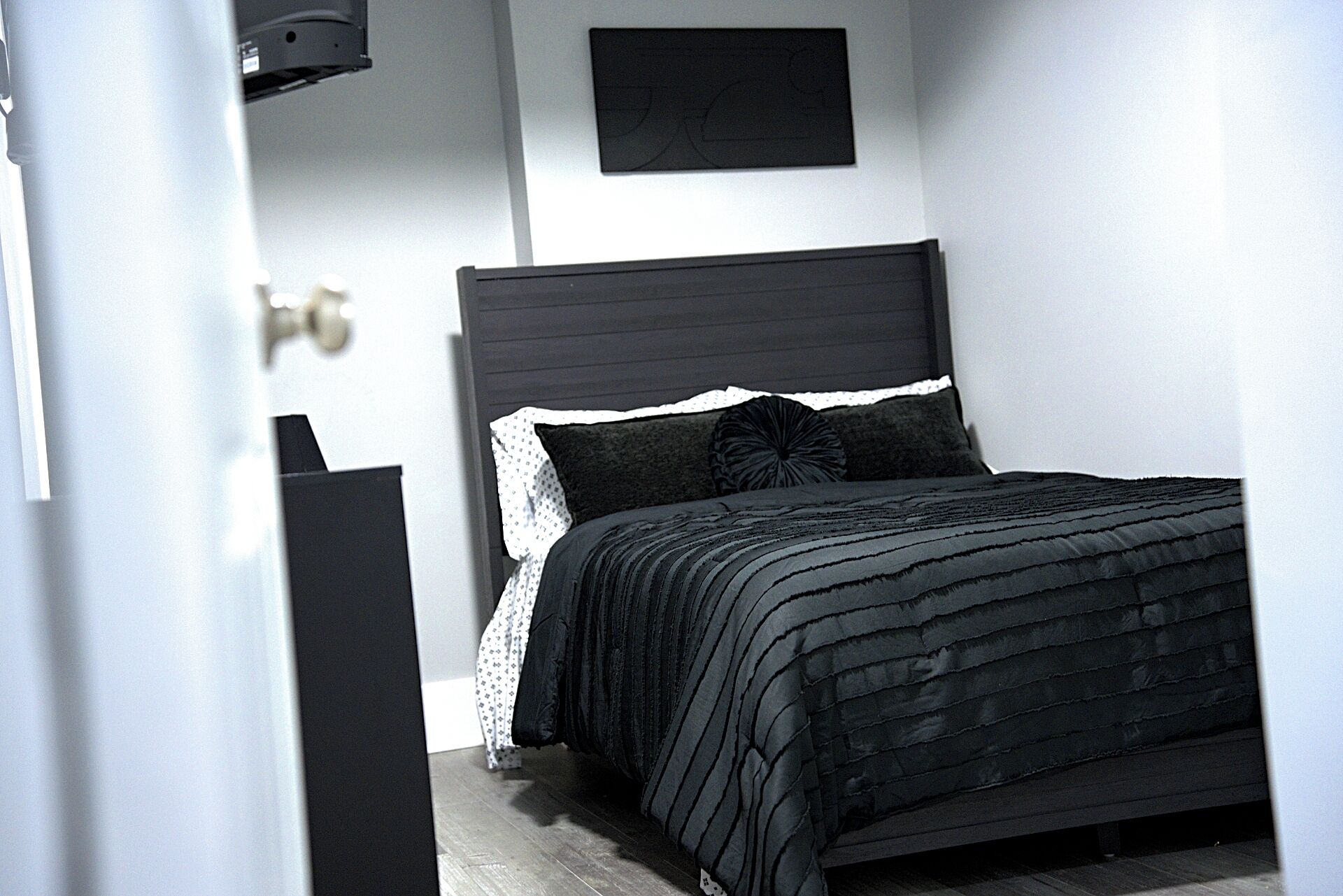 Una camera da letto con un letto di colore scuro, cuscini bianchi e neri e una testiera nera.