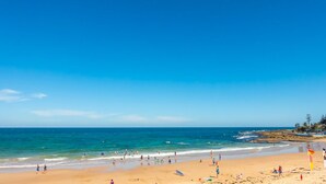 Une plage avec un ciel dégagé, une mer calme et des gens qui profitent du bord de mer.